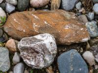Länglicher rotbrauner Stein mit weißen Einschlüssen neben weißbräunlichen Stein